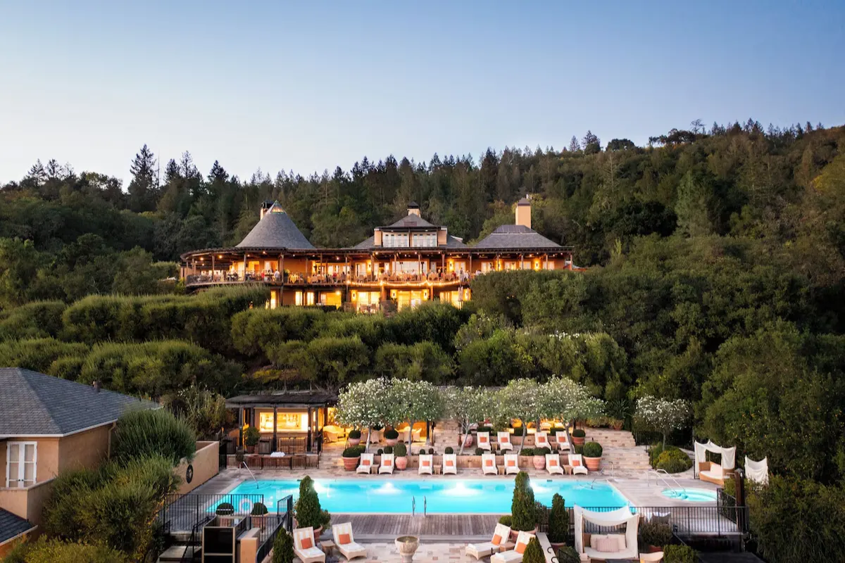 Auberge du Soleil lit at dusk on its wooded hillside above Rutherford, with the terrace pool in front