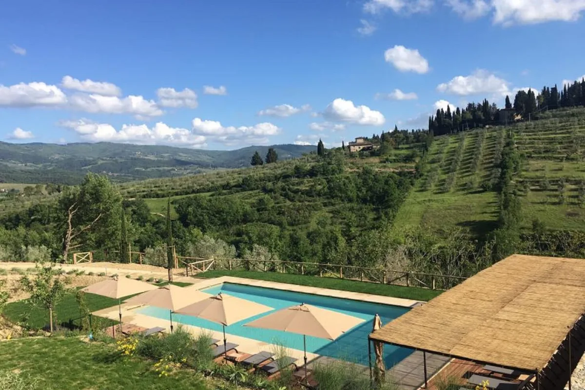 Rectangular swimming pool on a terrace above vineyard rows and wooded hills at Borgo del Cabreo, Greve in Chianti