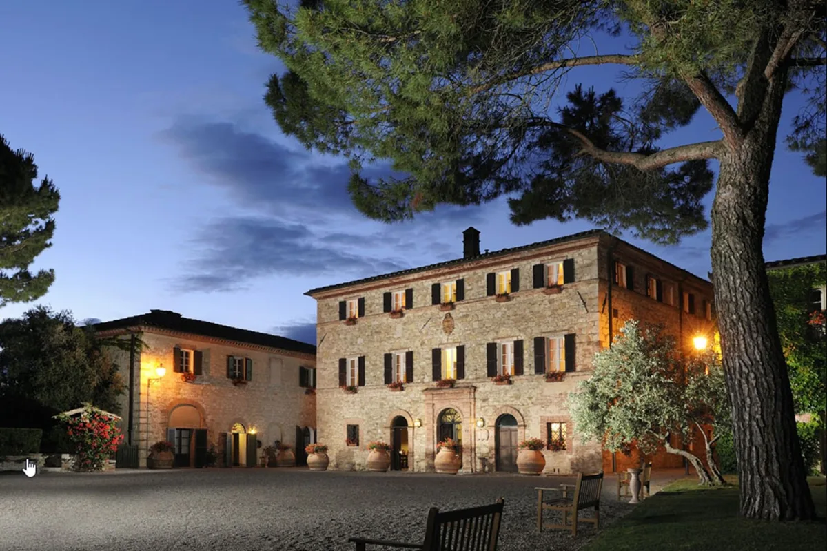 Stone hamlet buildings lit at dusk behind lawns and trees at Borgo San Felice, Castelnuovo Berardenga