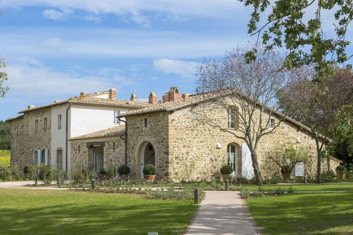 Long stone farmhouse with shuttered windows and a lawn under a Tuscan sky at Podere Brizio, west of Montalcino