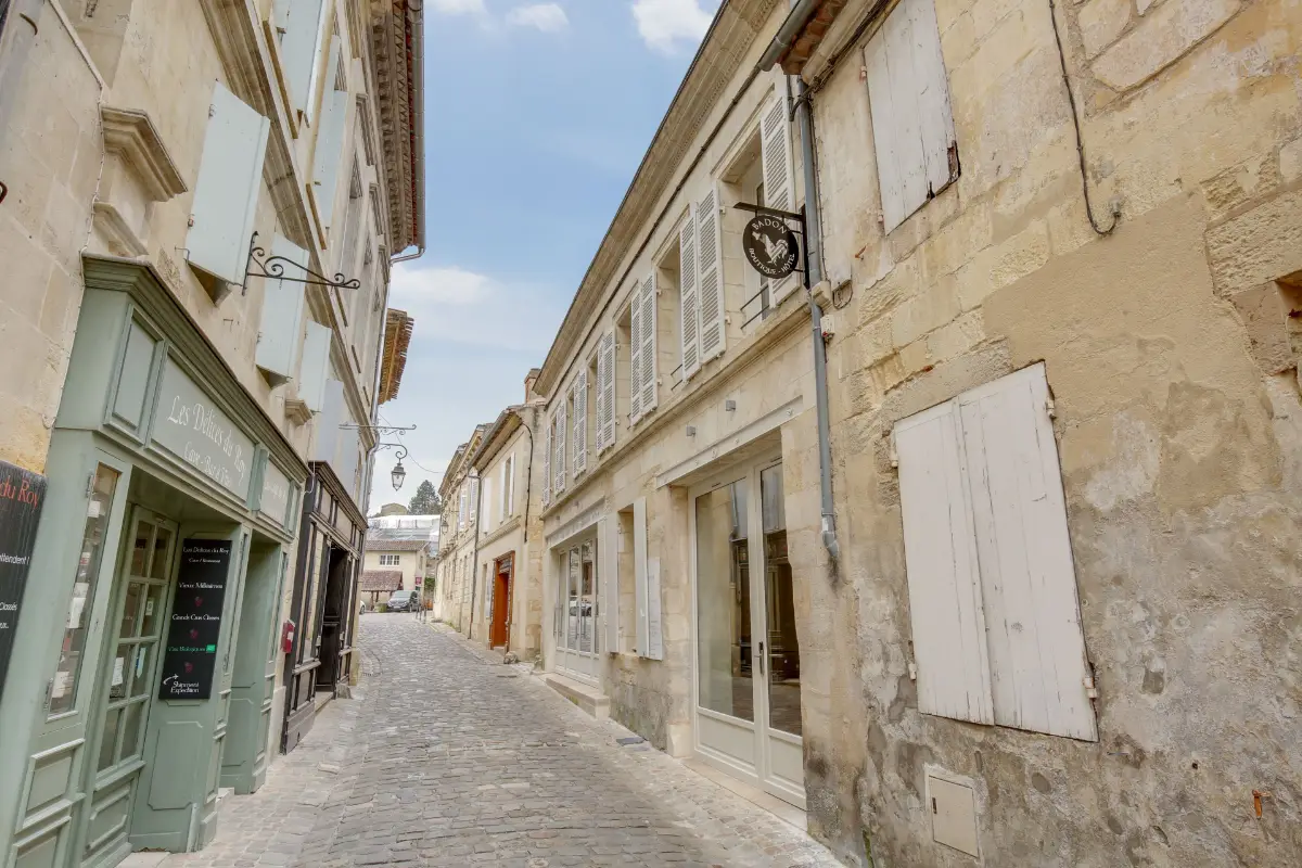 A narrow limestone lane in Saint-Émilion with shuttered windows and the green shopfront of Badon Boutique Hôtel