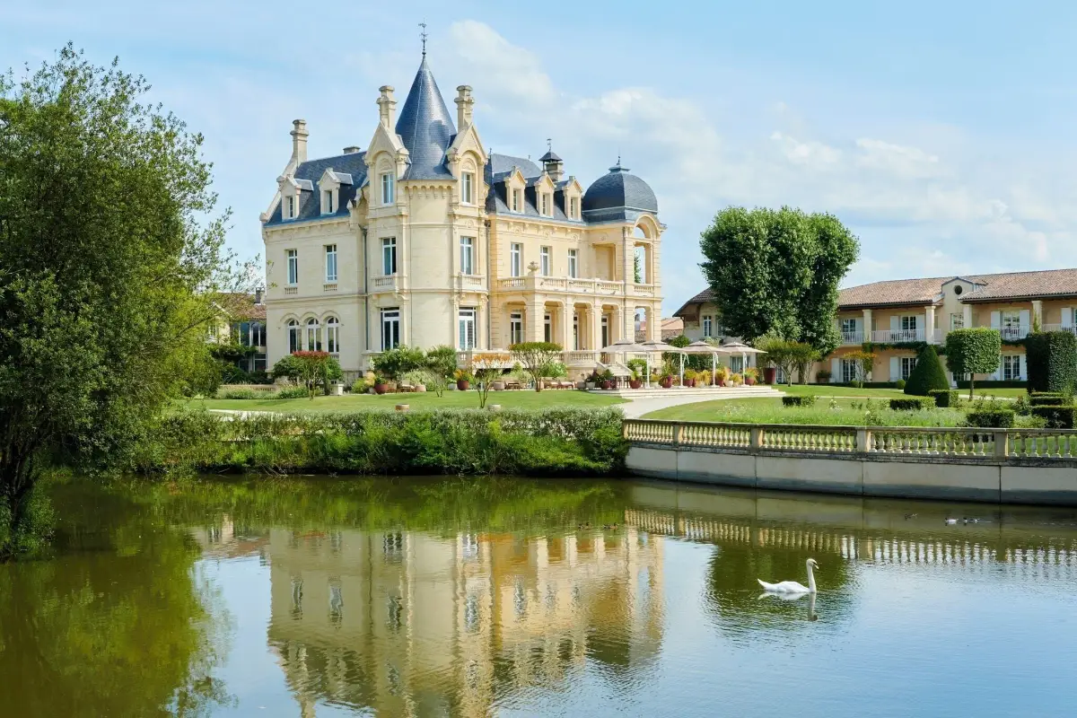 Château Hôtel Grand Barrail reflected in its lake, with the park and the vines of Saint-Émilion around it