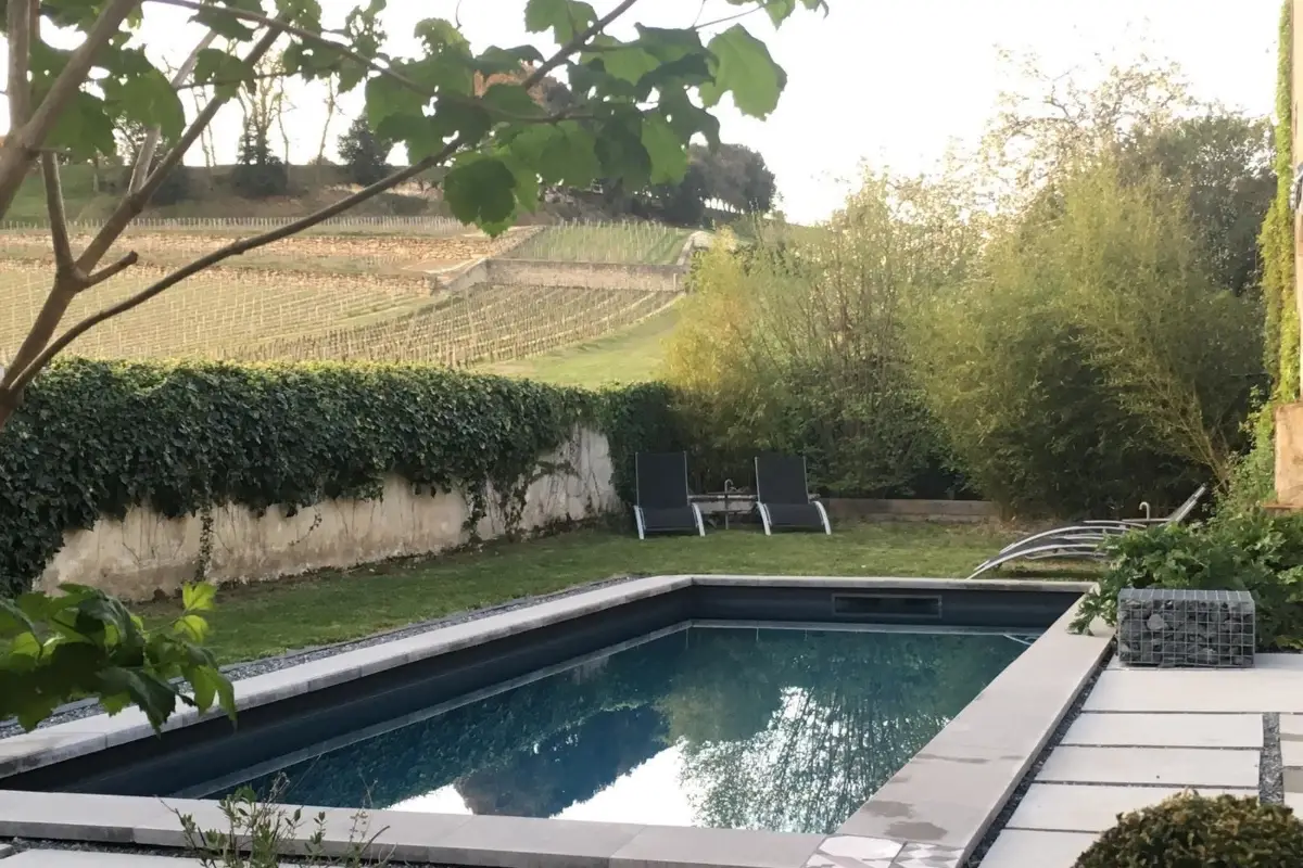 The outdoor pool at Clos 1906, enclosed by a stone wall with the vineyard slope rising beyond it