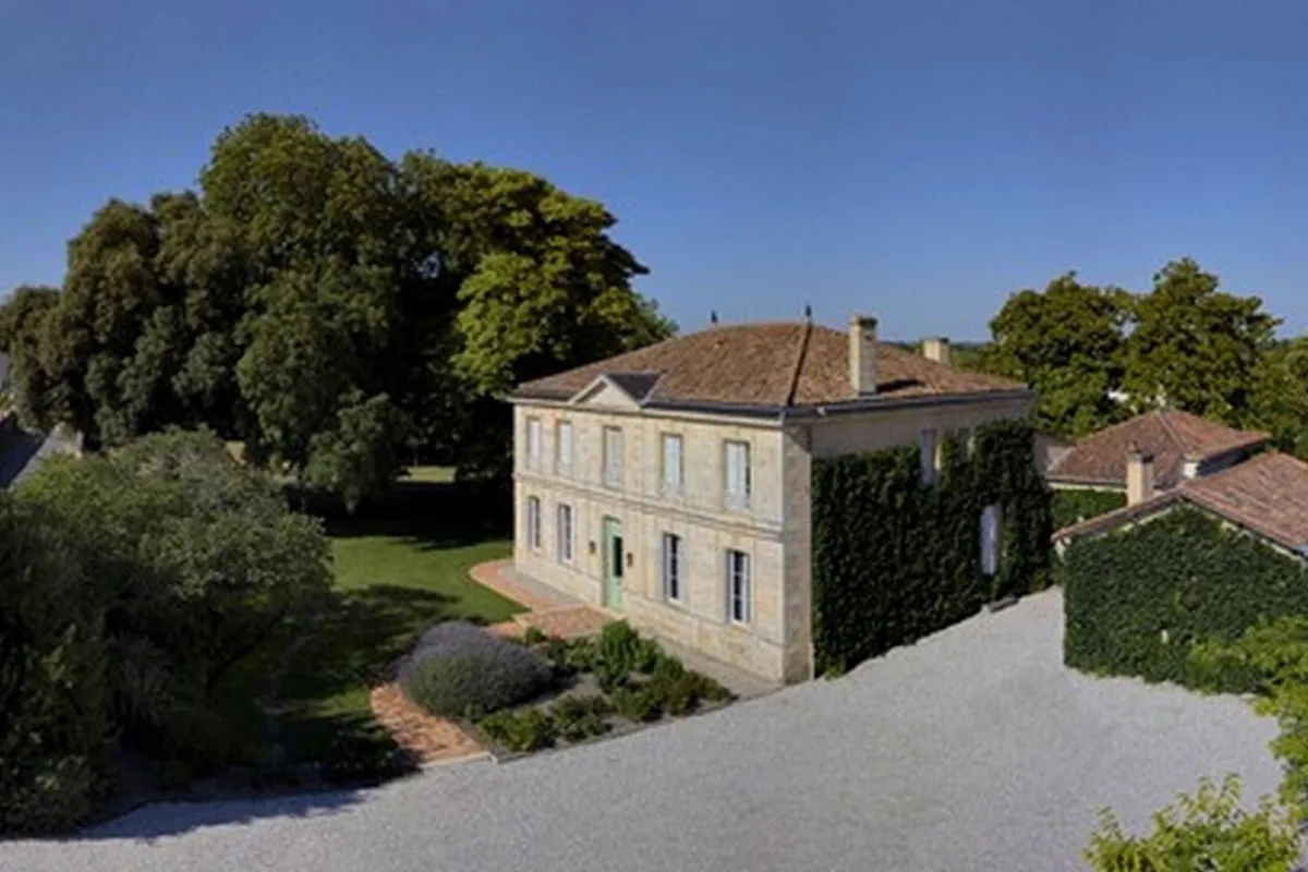 Château Ormes de Pez from the air: stone estate buildings among trees with the Saint-Estèphe vines behind them