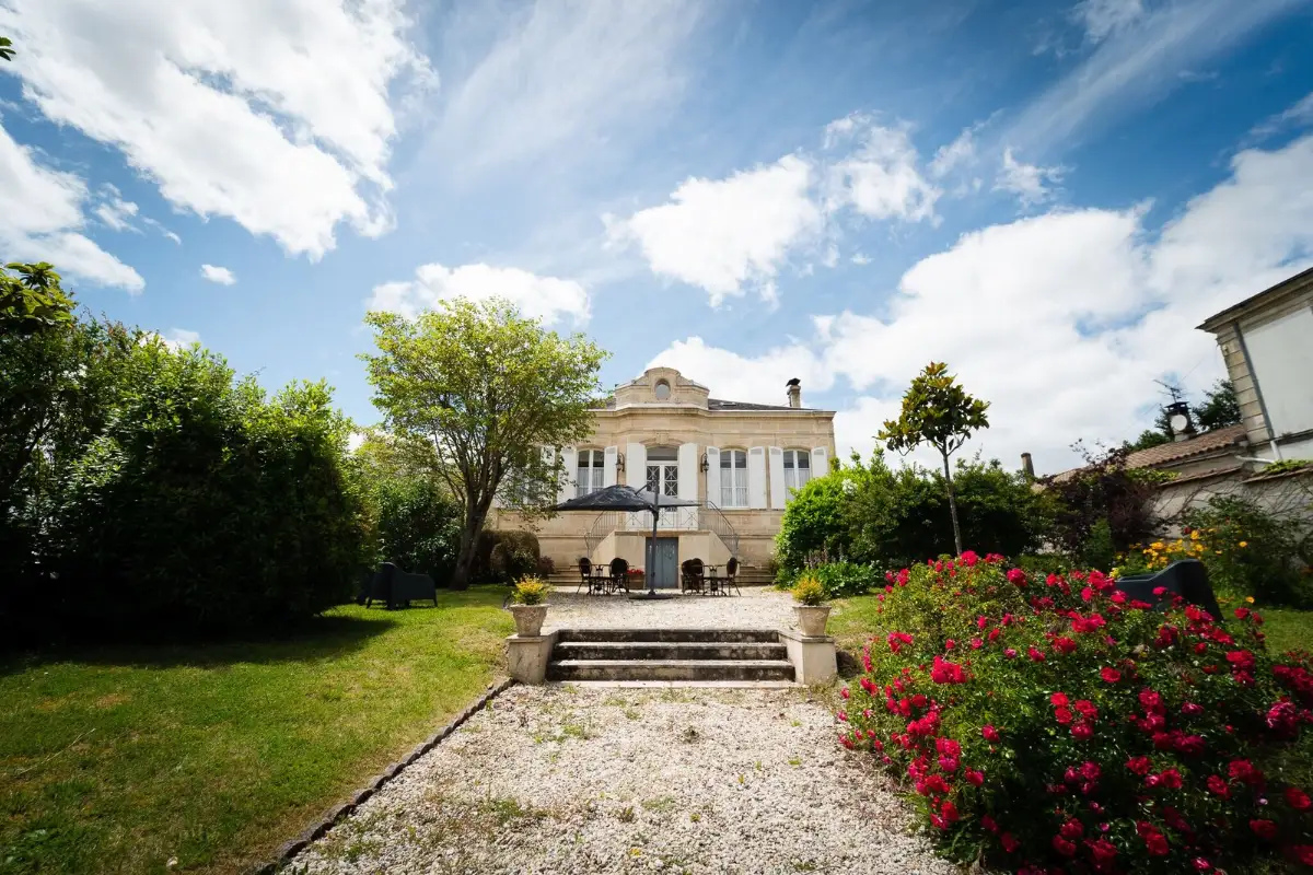 The white pedimented front of Château Papounan in Saint-Estèphe, above a stone staircase with roses on the lawn