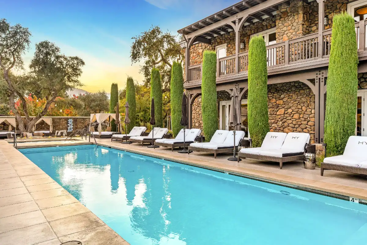 The pool at Hotel Yountville lined with white loungers and cypress trees, one of the six hotels in this guide to where to stay in Yountville
