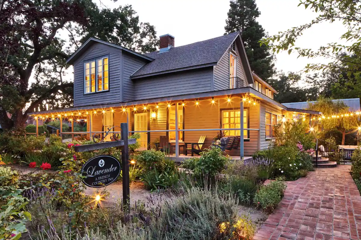 The lit porch and flower garden of the clapboard farmhouse at Lavender, A Four Sisters Inn in Yountville, at dusk