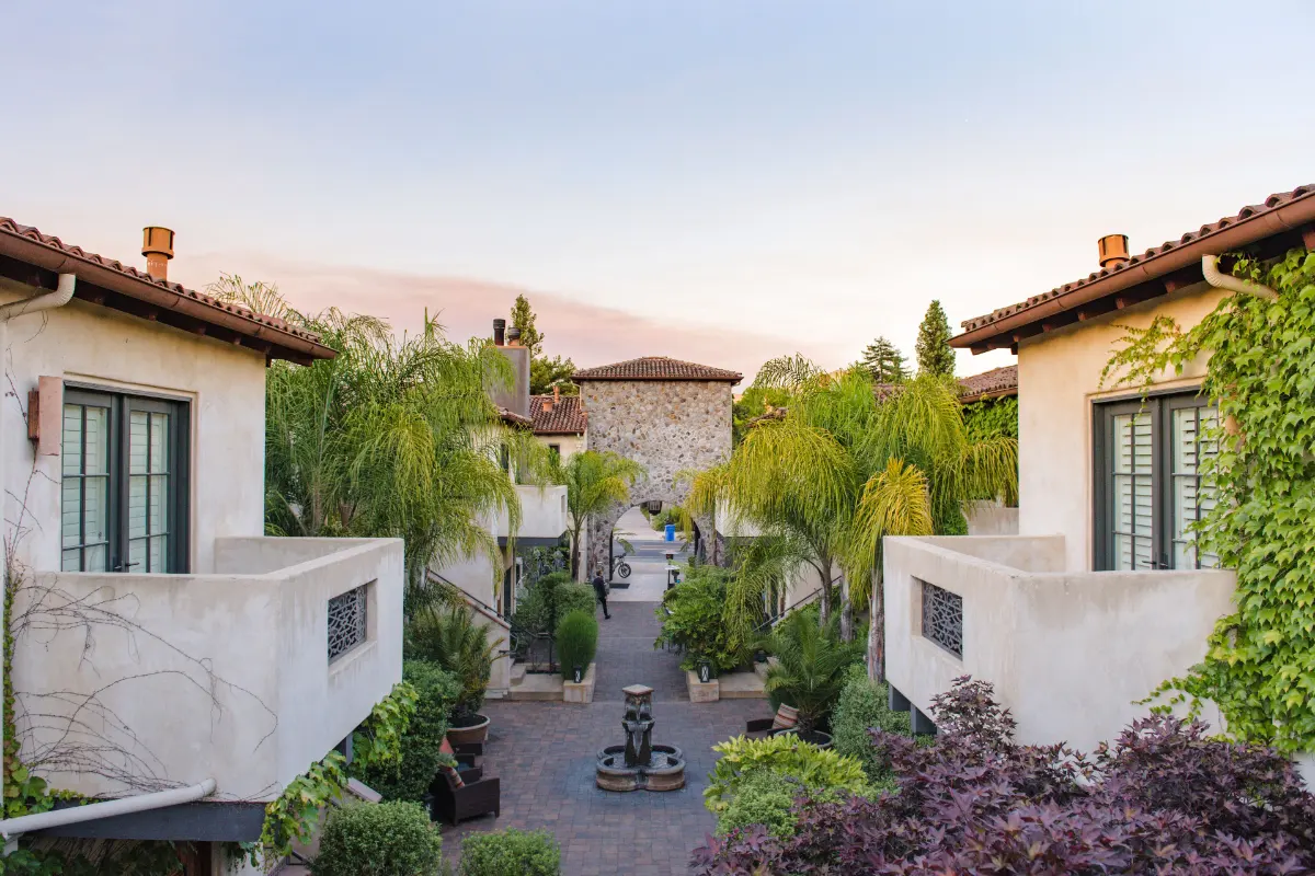 Planted courtyard with a stone fountain between the stucco buildings and palms of North Block Hotel in Yountville at dusk