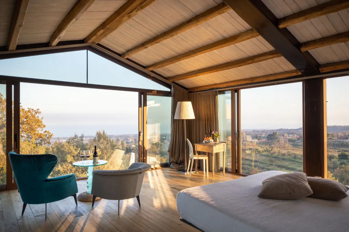 A suite with glass walls and a wooden ceiling at Monaci delle Terre Nere, looking out toward the sea