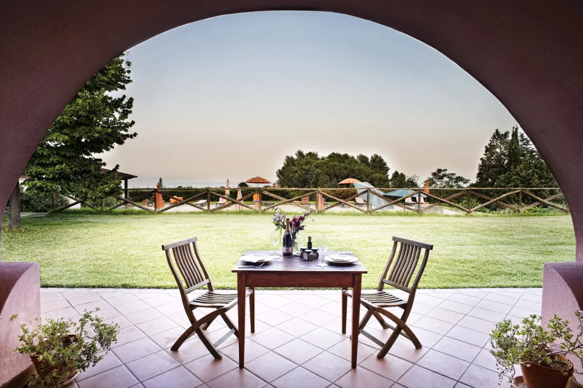 A table for two under a stone arch facing the lawn at Tenuta San Michele in Santa Venerina