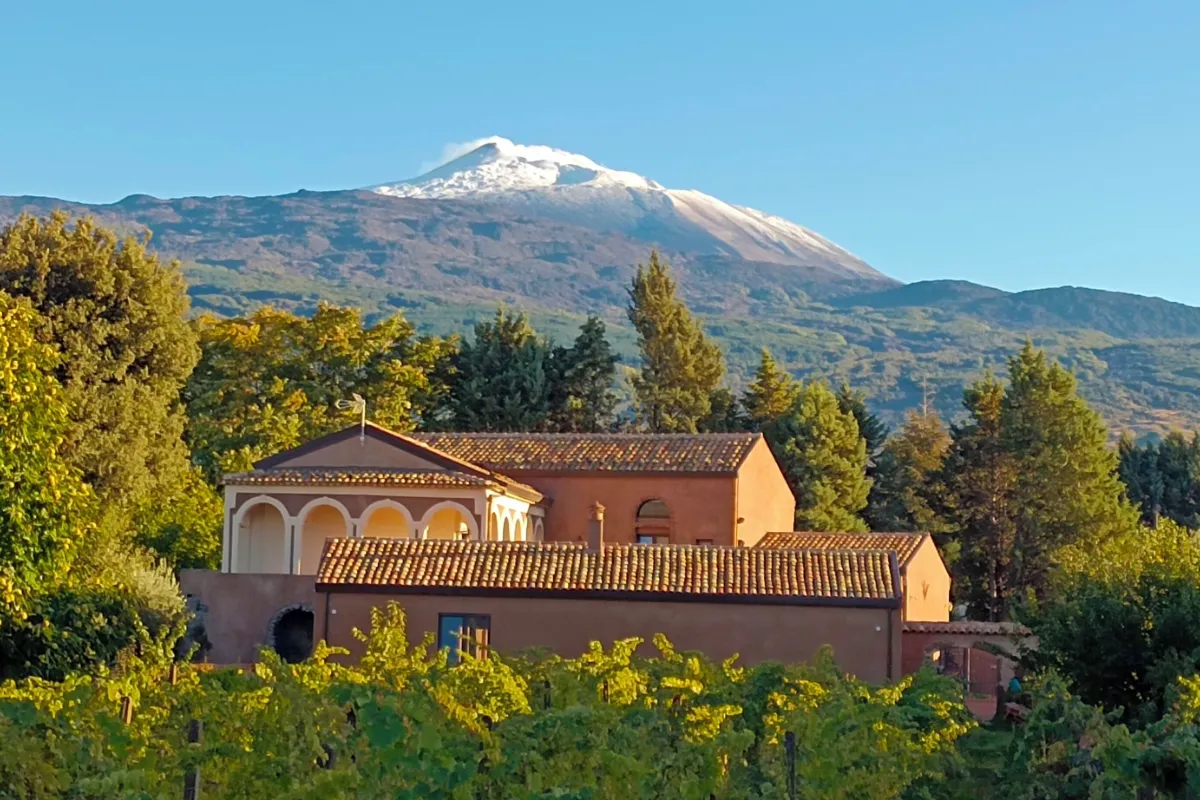 Casale Dilettoso Etna Relais near Randazzo, a stone farmhouse among trees below snow-capped Mount Etna