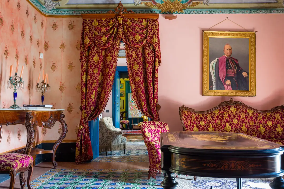 Period salon at Palazzo Previtera in Linguaglossa, with red drapes, an antique sofa and a family portrait