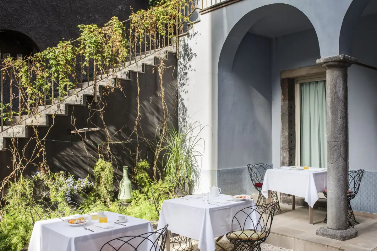 Garden terrace with stone arches and dining tables at Shalai in Linguaglossa