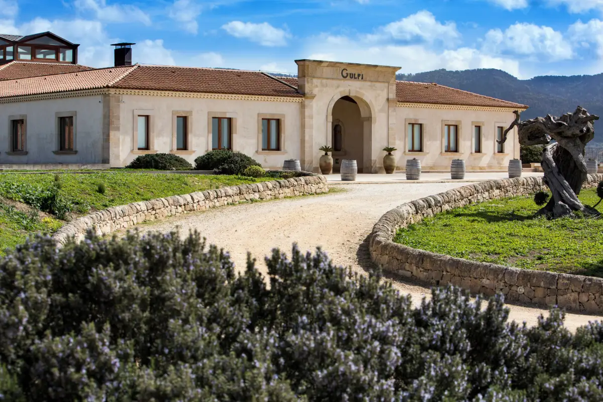 Stone estate building and garden path at Locanda Gulfi in Chiaramonte Gulfi, with hills behind