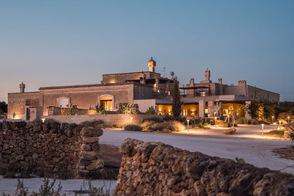 The stone buildings of Masseria Cuturi near Manduria lit up at dusk, behind a dry-stone wall