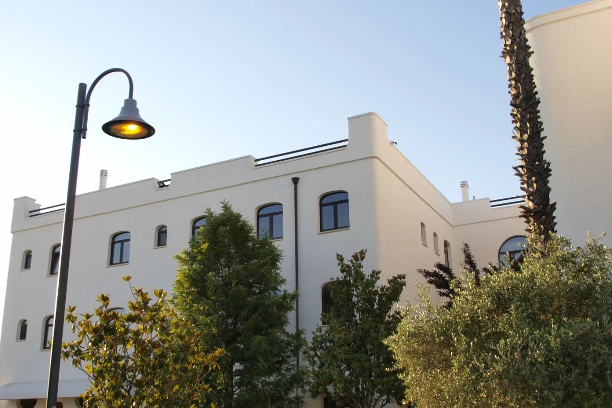 White facade of the Leone de Castris Wine Hotel in Salice Salentino, with a street lamp and garden trees