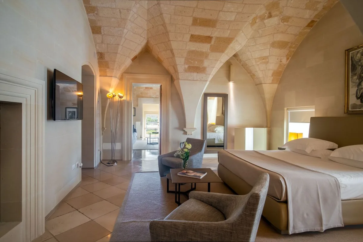 Bedroom at La Fiermontina in Lecce under pale stone cross vaults, with armchairs and an open doorway to a further room