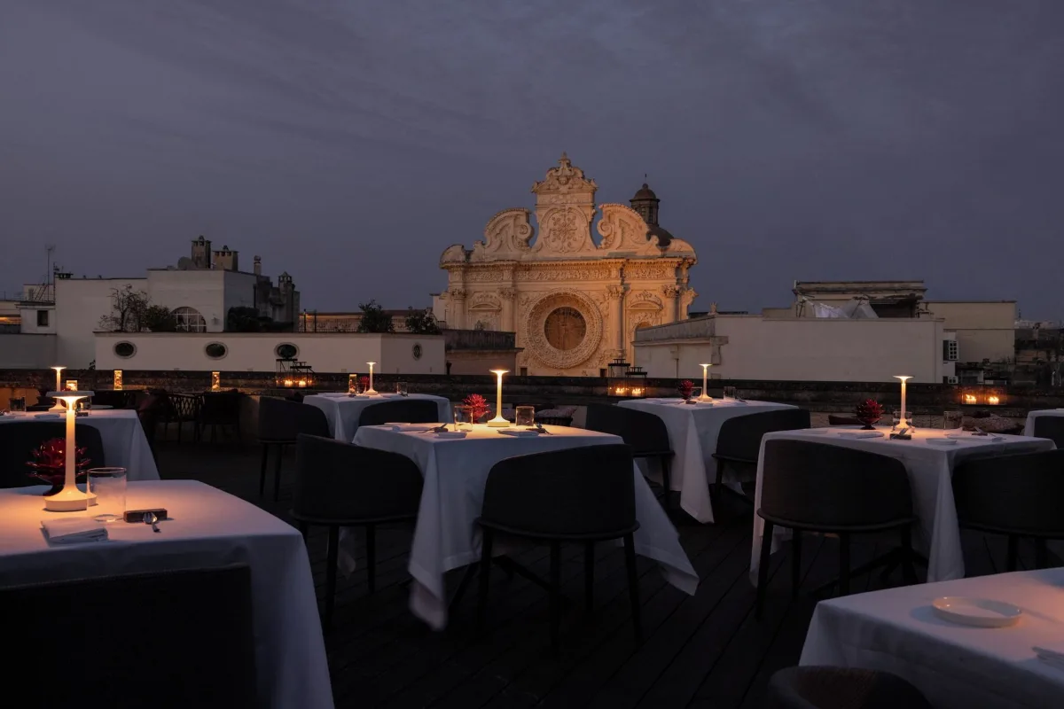 Best hotels in Lecce: candlelit rooftop tables at Patria Palace facing the baroque facade of the Basilica di Santa Croce at dusk