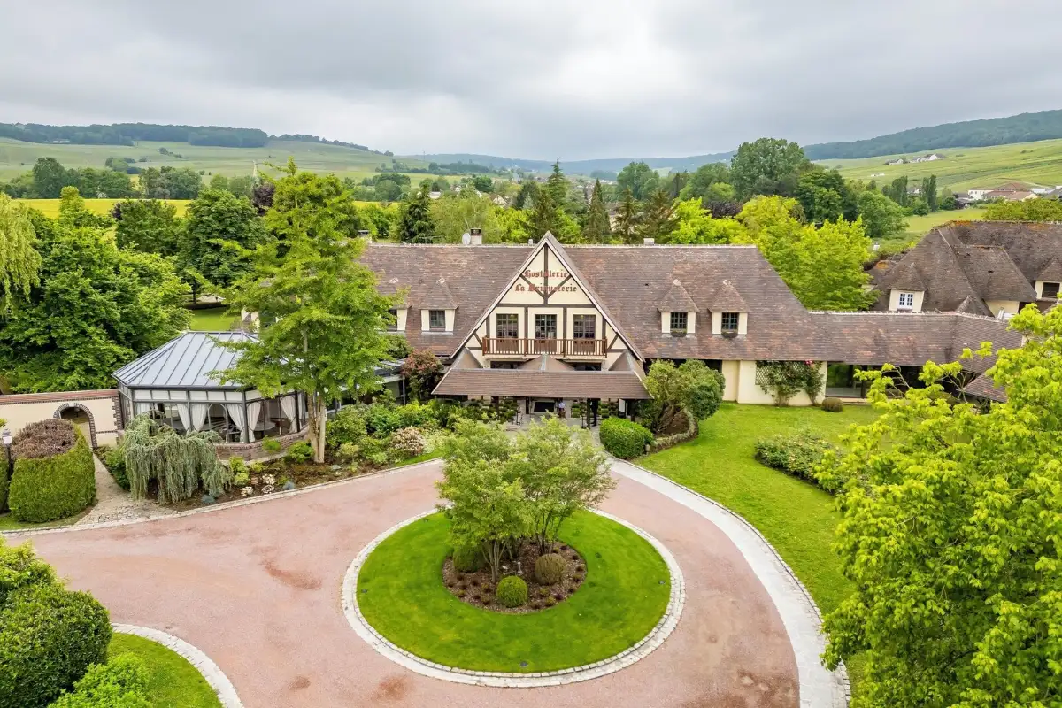 Aerial view of Briqueterie Champagne in Vinay: a half-timbered house in gardens with vineyard hills behind