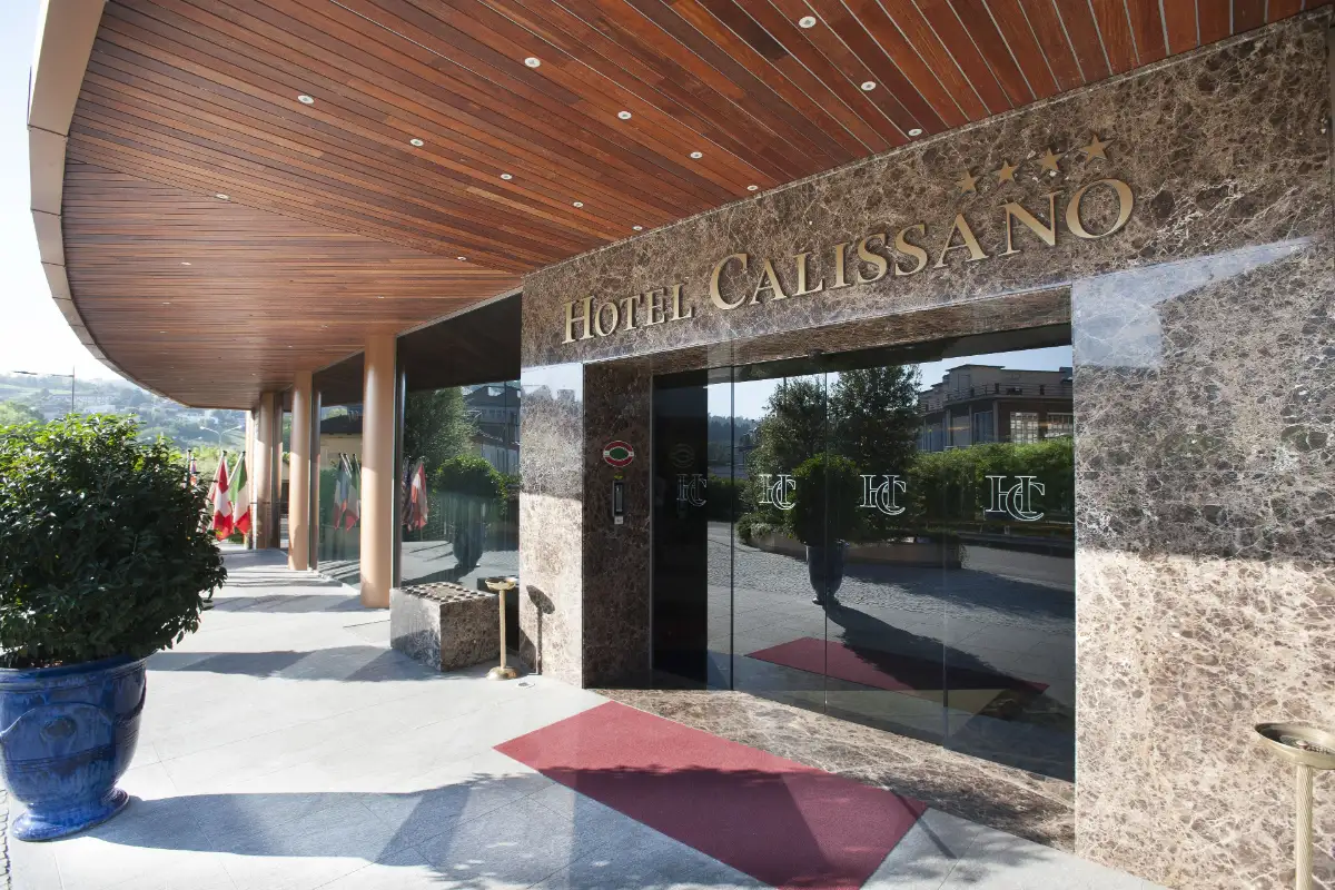Entrance of Hotel Calissano in Alba under a curved wooden canopy with a stone facade