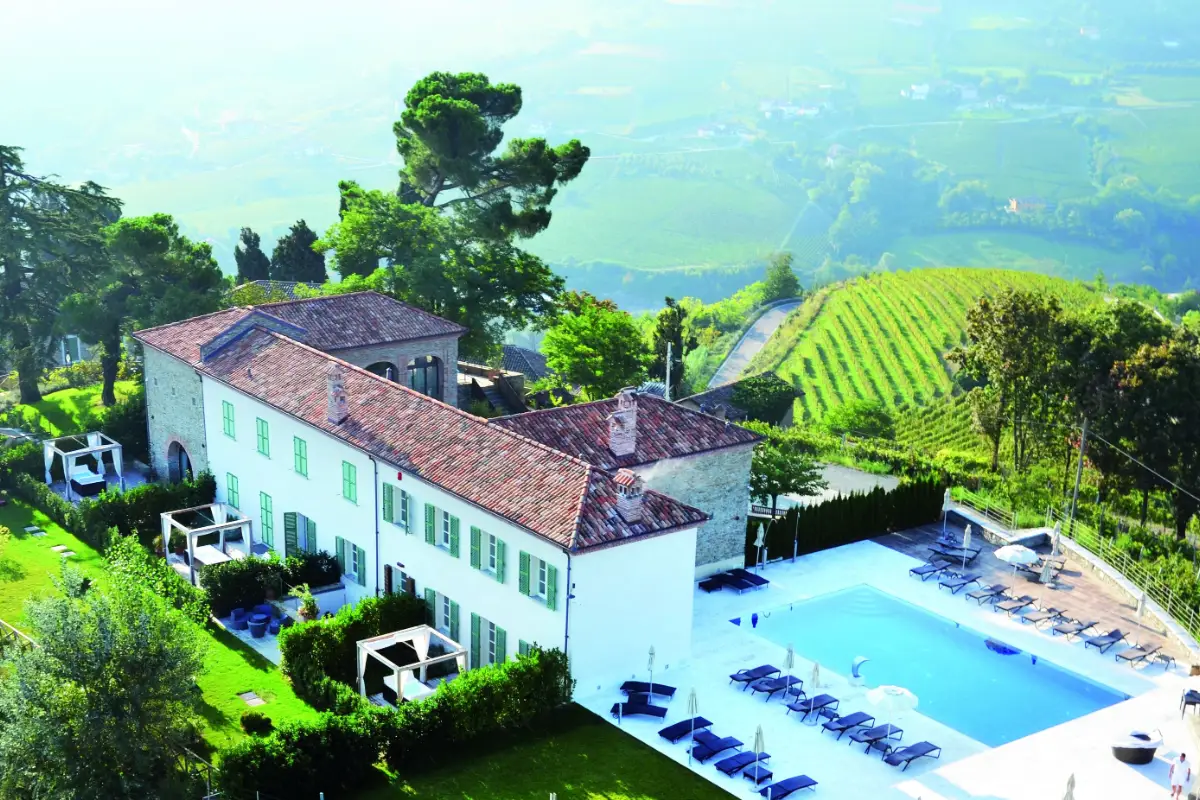Aerial view of Relais San Maurizio, a white building with a pool among trees and vineyards