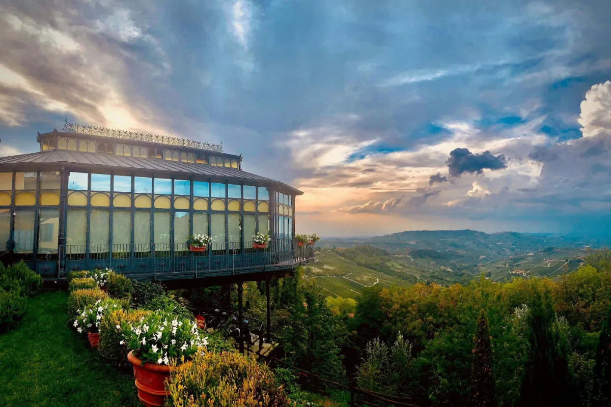 Glass-roofed pavilion at Hotel Villa Beccaris with flower boxes and a view over the Langhe hills at sunset